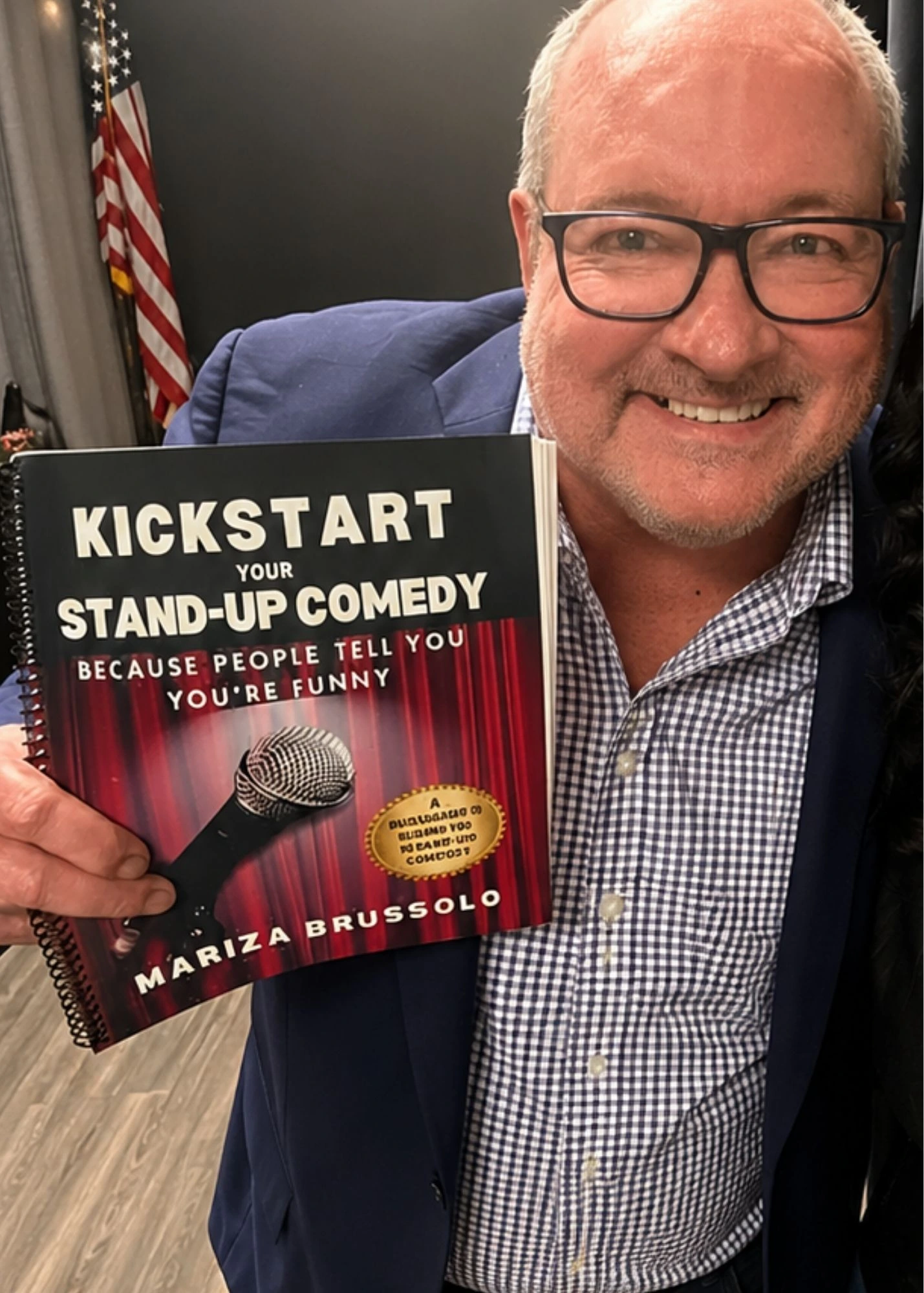 Man holding a copy of Kickstart Your Stand-Up Comedy by Mariza Brussolo