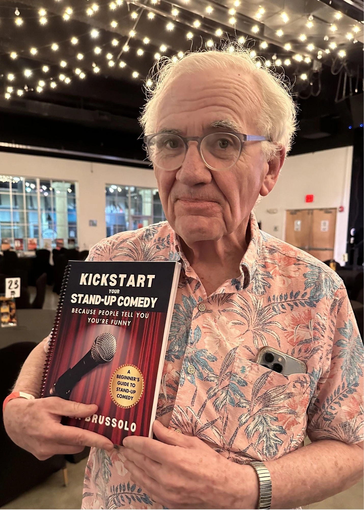 Man holding a copy of Kickstart Your Stand-Up Comedy by Mariza Brussolo