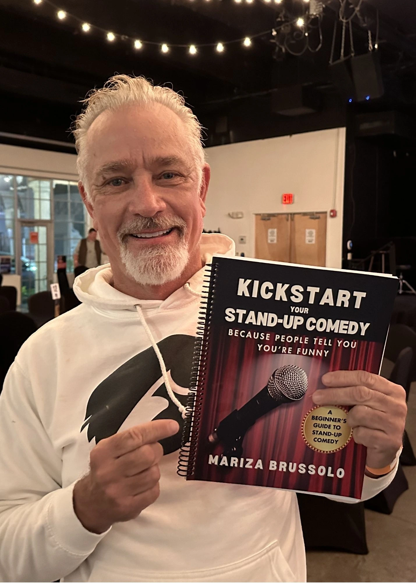 Man holding a copy of Kickstart Your Stand-Up Comedy by Mariza Brussolo