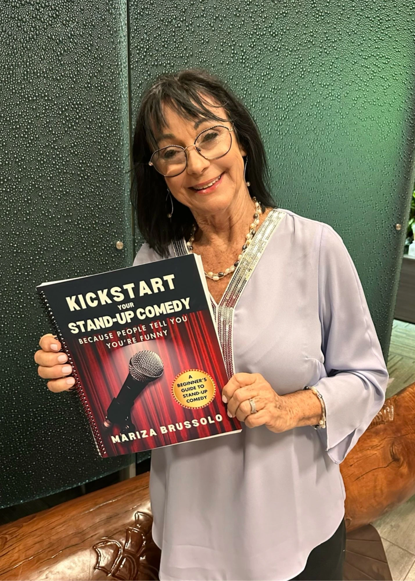Woman holding a copy of Kickstart Your Stand-Up Comedy by Mariza Brussolo