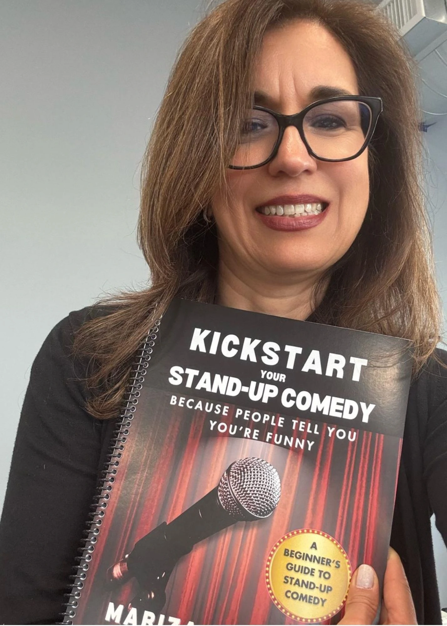 Woman holding a copy of Kickstart Your Stand-Up Comedy by Mariza Brussolo