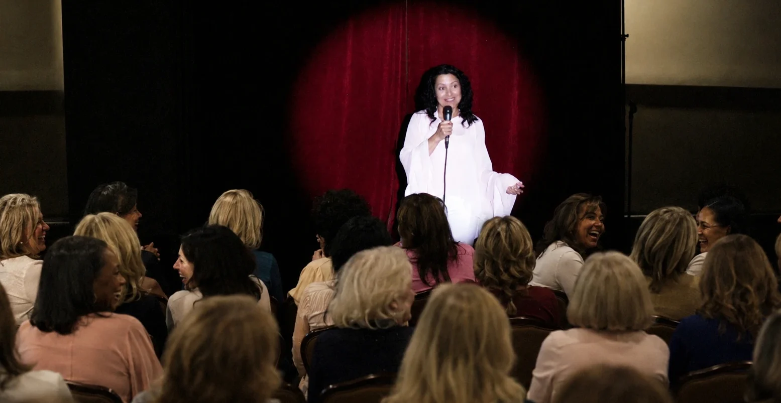 comedian on stage performing for women in the audience laughing