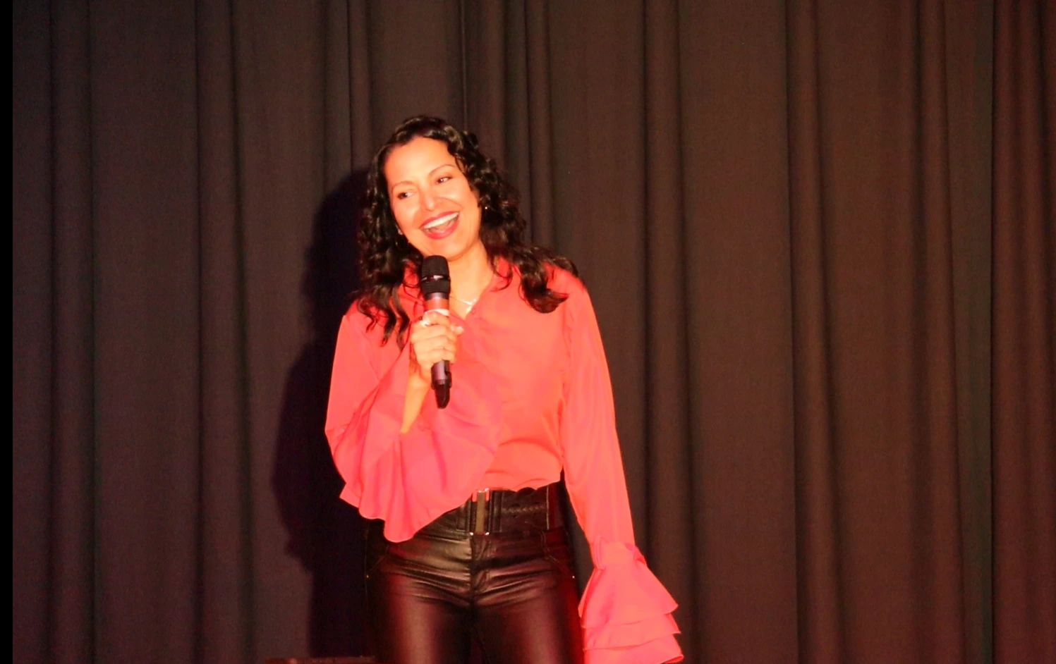 woman on stage holding a mic wearing red blouse smiling