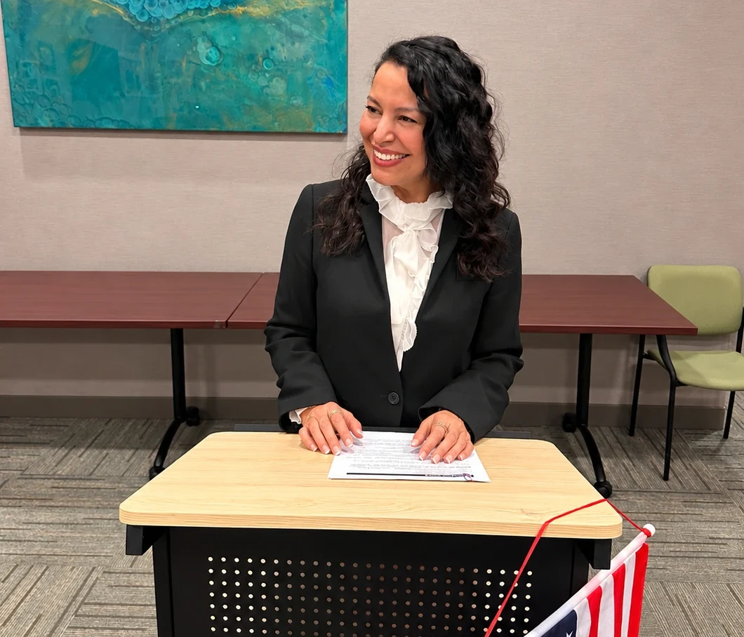 woman wearing a black blazer white blouse standing behind a lectern smiling